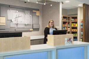 Un mostrador de recepción de hotel con una computadora, un cartel de Holiday Inn Express & Suites, y una exhibición de bocadillos y bebidas.