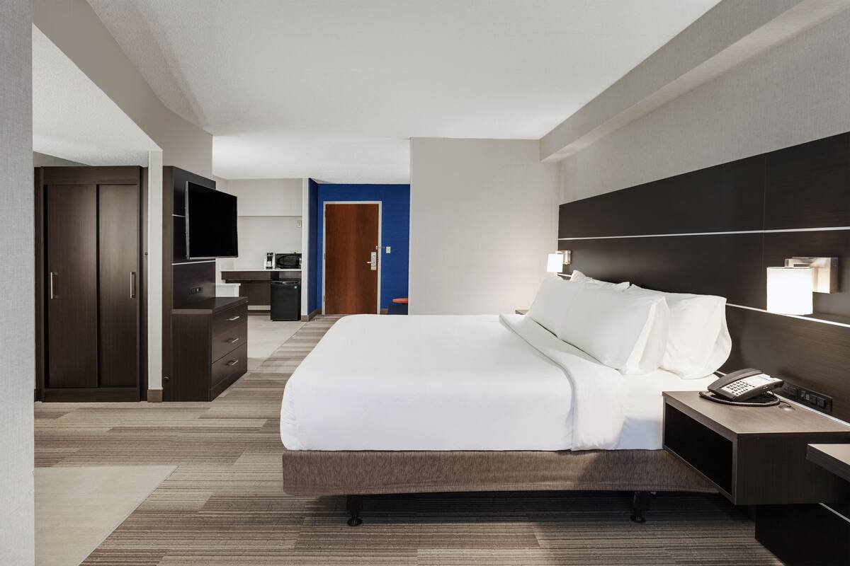 Una habitación de hotel moderna con una cama grande, una mesita de noche con teléfono, un televisor montado en la pared, un armario y un escritorio con silla.