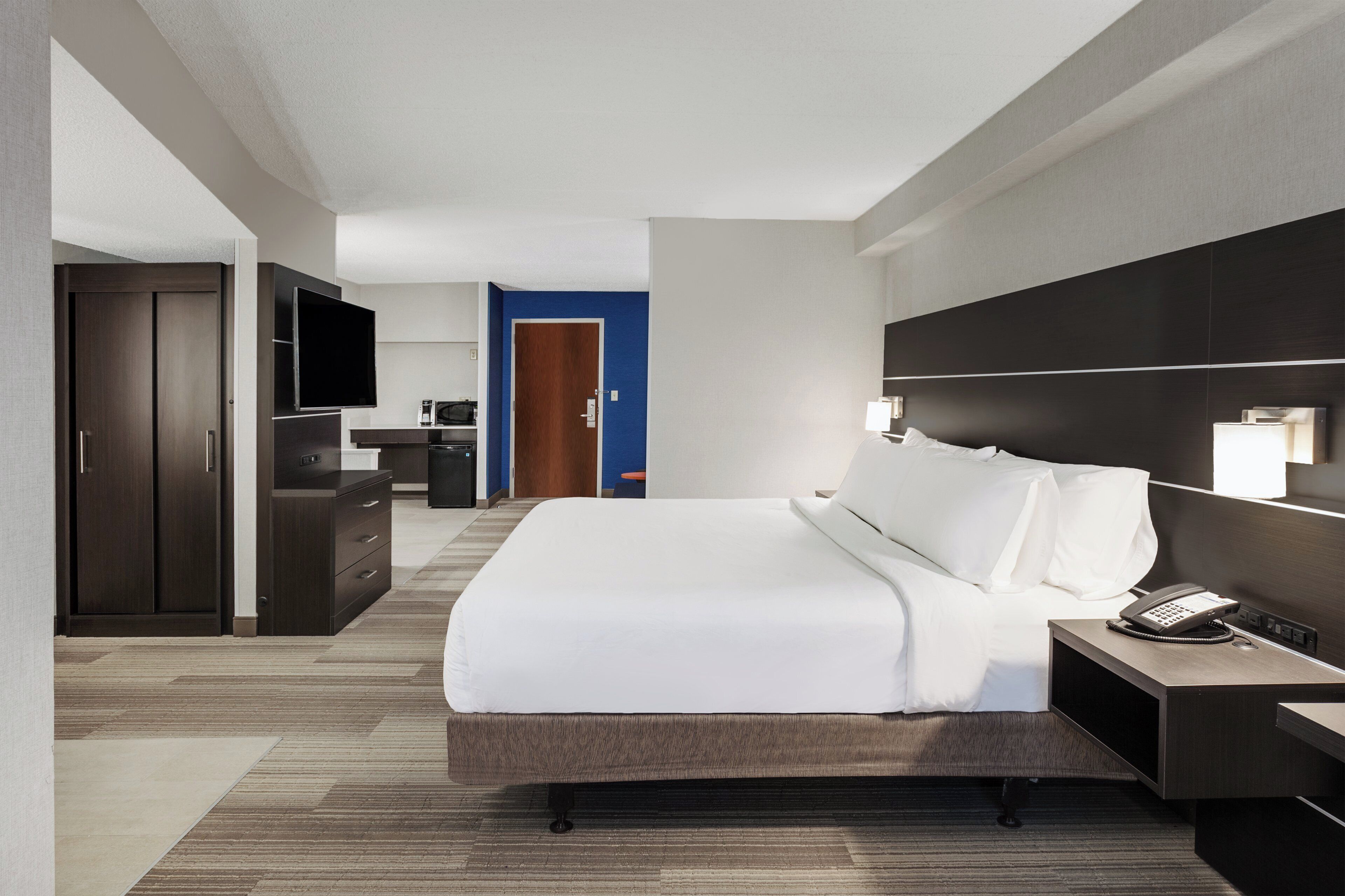 Una habitación de hotel con una cama grande, un escritorio con teléfono, una televisión y un armario.