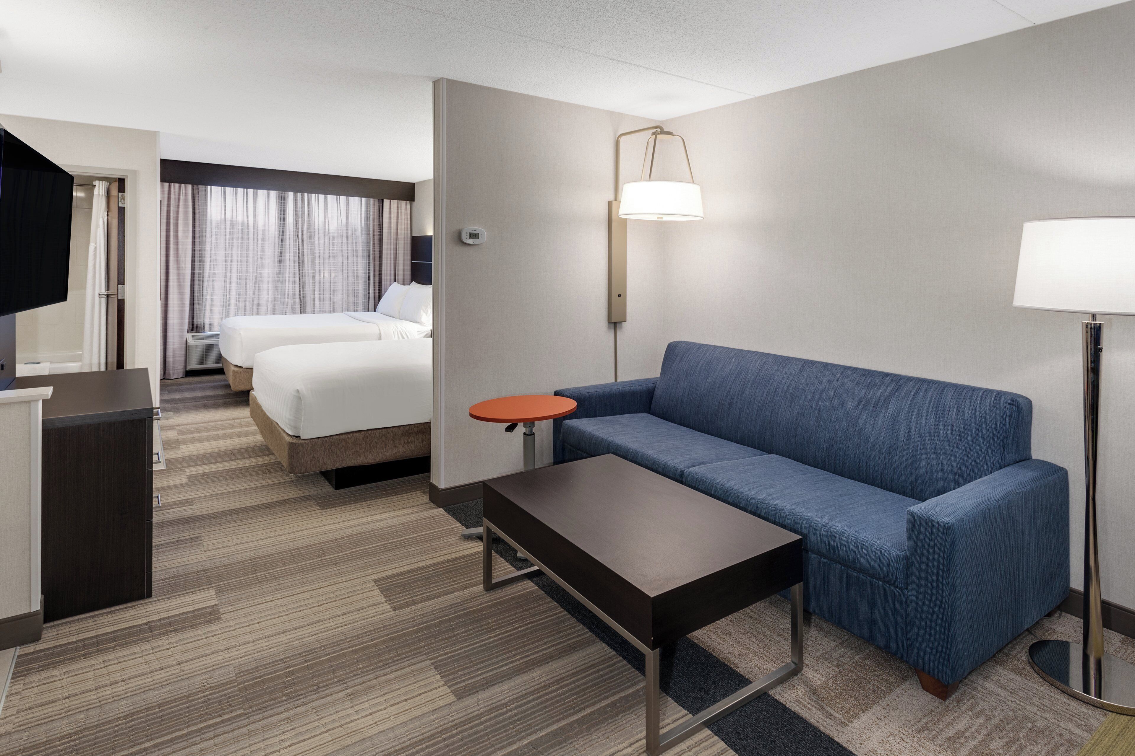 A hotel room with a bed, a sofa, a small table, a TV, and a lamp.