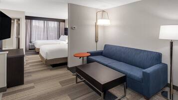 A hotel room with a bed, a sofa, a small table, a TV, and a lamp.