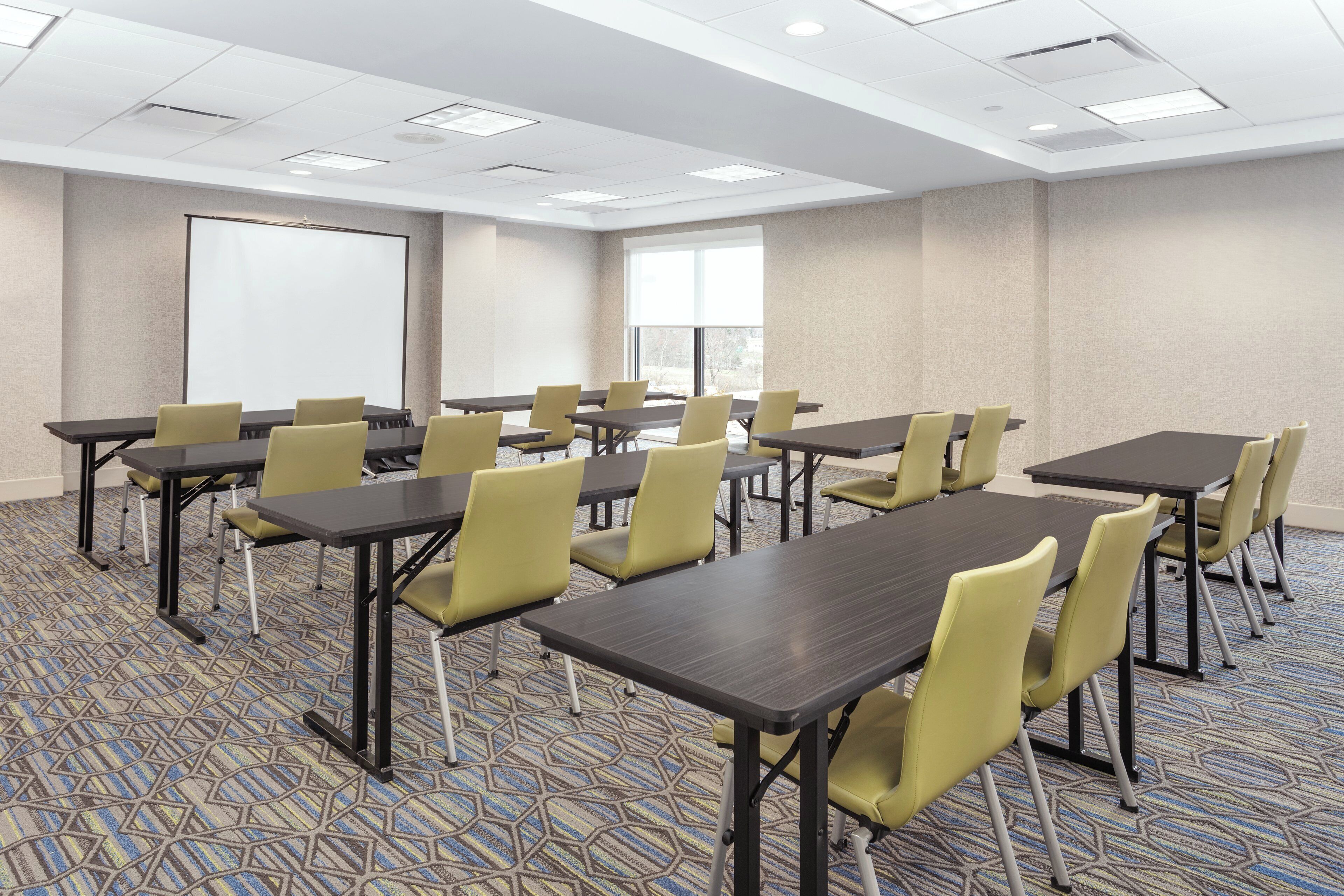A conference room with multiple tables and chairs, a projection screen, and a large window.