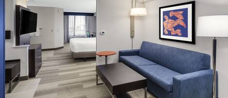 Una habitación de hotel moderna con sofá, una mesa de centro, televisor, escritorio y cama.