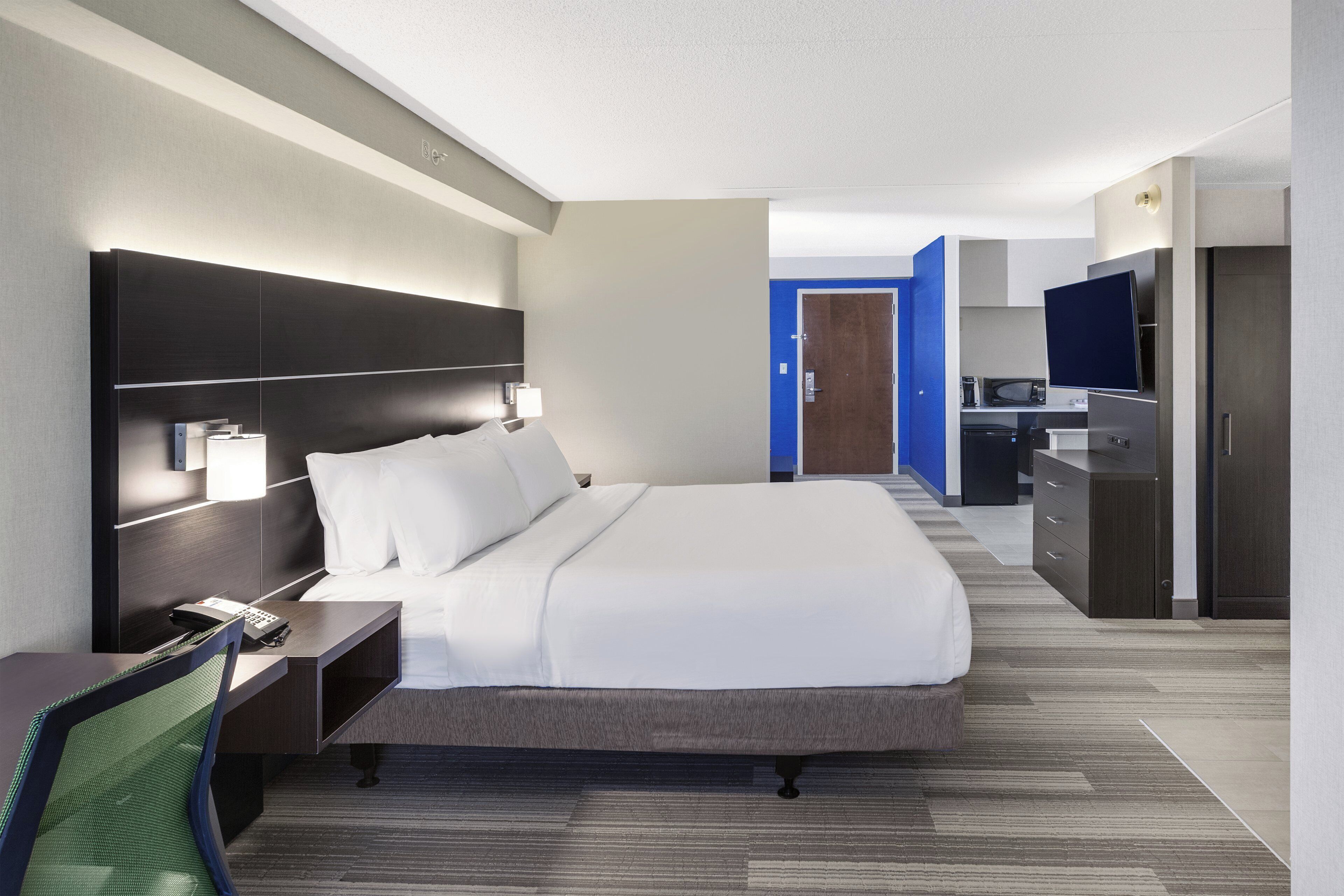 Ein Hotelzimmer mit einem großen Bett, Nachttischen, einem Schreibtisch, einem Sessel und einem Kleiderschrank. Ein Badezimmer ist durch eine geöffnete Tür zu sehen.