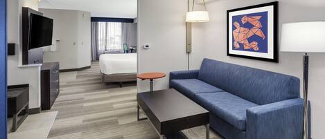 Een hotelkamer met een bank, een eettafel, een televisie, een bed en een schilderij aan de muur.