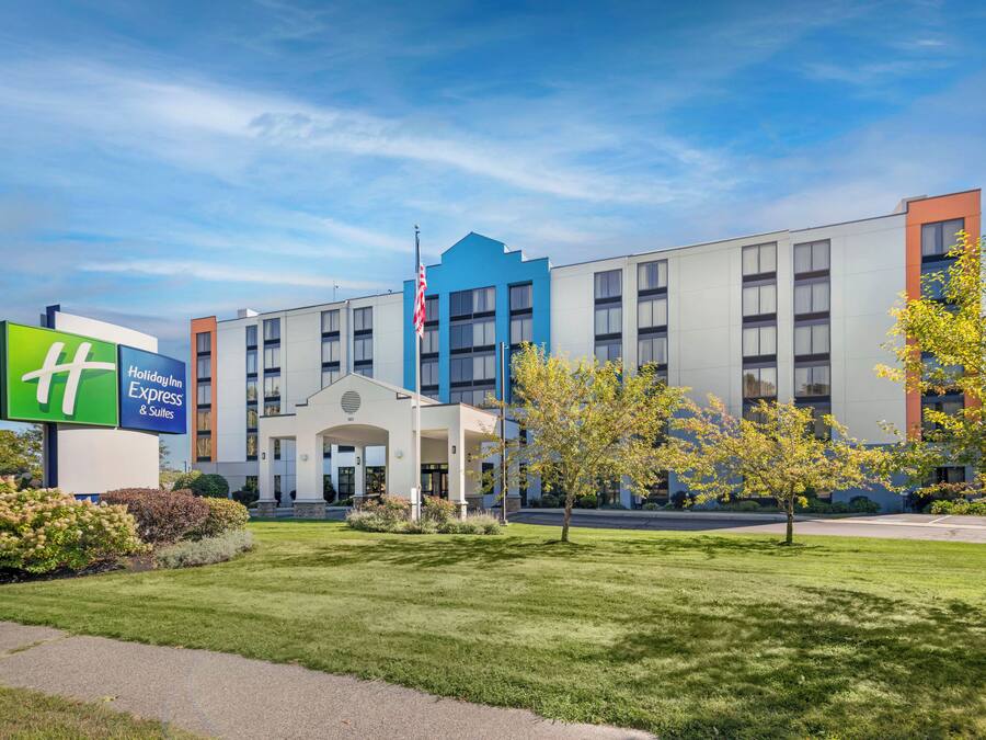 A Holiday Inn Express & Suites hotel with a modern design, featuring a large sign, a flag, and well-maintained landscaping.