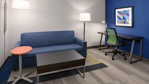 Une chambre d’hôtel moderne avec un canapé bleu, une petite table ronde, un bureau avec une chaise et deux lampadaires.