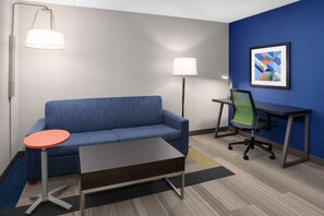 A modern hotel room with a blue sofa, a small round table, a desk with a chair, and two floor lamps. - Holiday Inn Express Hotel & Suites South Portland by IHG (South Portland)