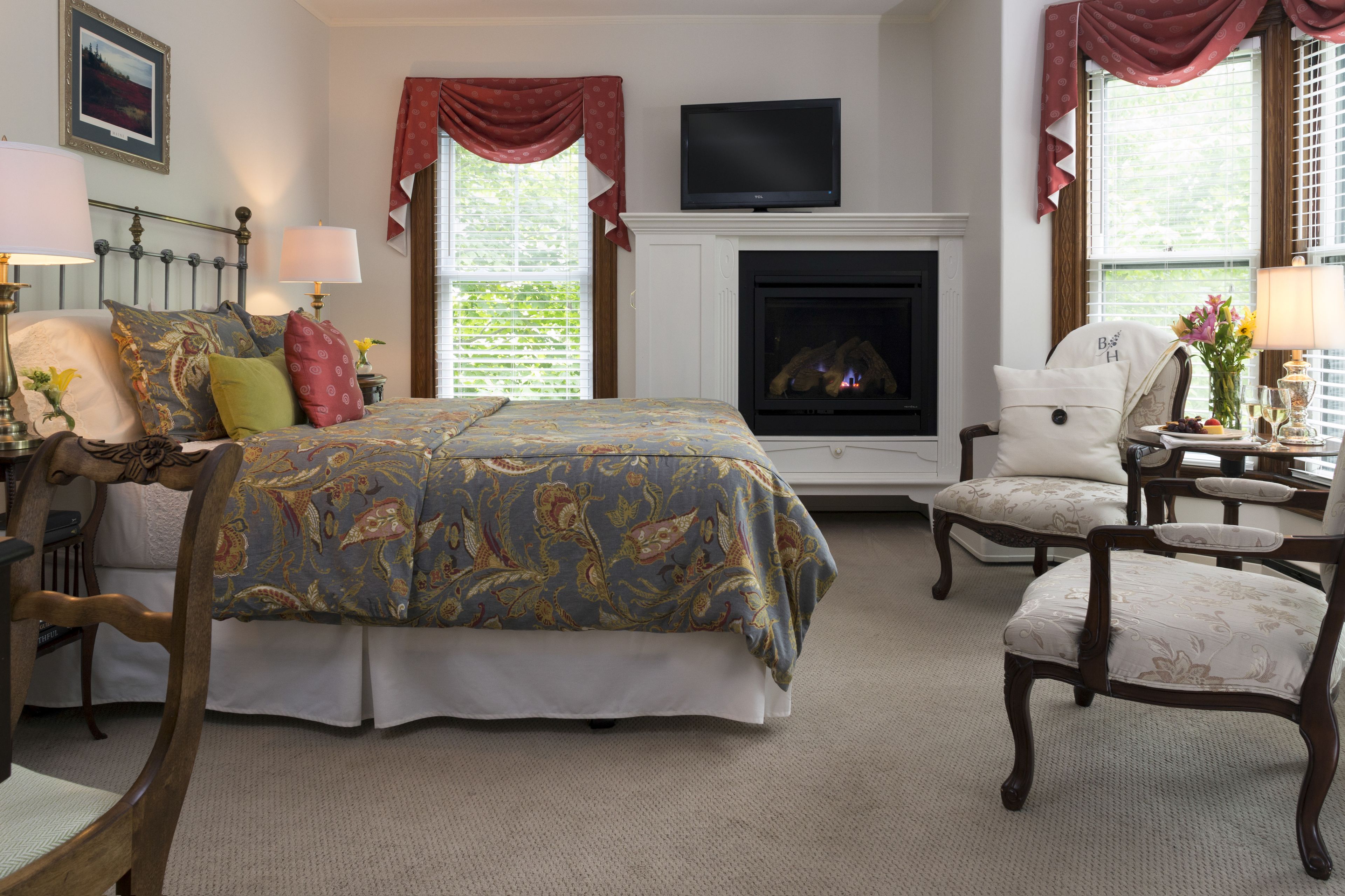 A bedroom with a bed, a television above the fireplace, and a chair.