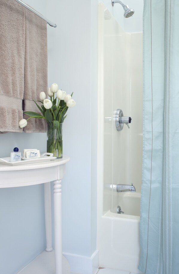 A bathroom with a white sink, a mirror, a towel rack with a towel, a glass vase with flowers, and a shower area with a glass door.