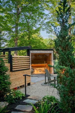 A wooden outdoor seating area with a bench and a table, surrounded by trees and plants.