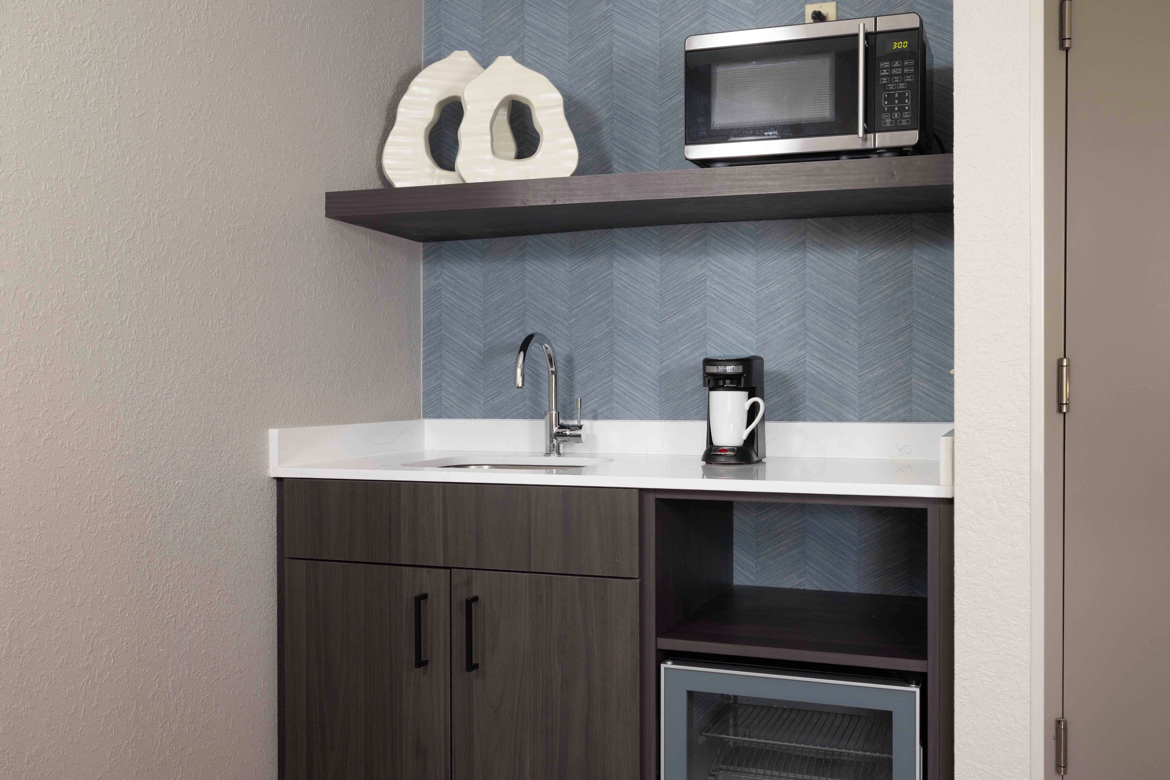 Een kitchenette met een magnetron, koffiezetapparaat en een spoelbak.