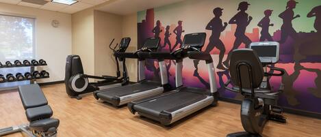 A gym with treadmills, dumbbells, and a wall mural of runners.