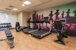 A gym with treadmills, dumbbells, and a wall mural of runners. - Hyatt Place Boston/Medford (Medford)