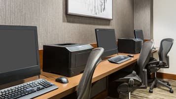 Espaço de trabalho em hotel com três estações de computador, cada uma equipada com monitor, teclado e rato.