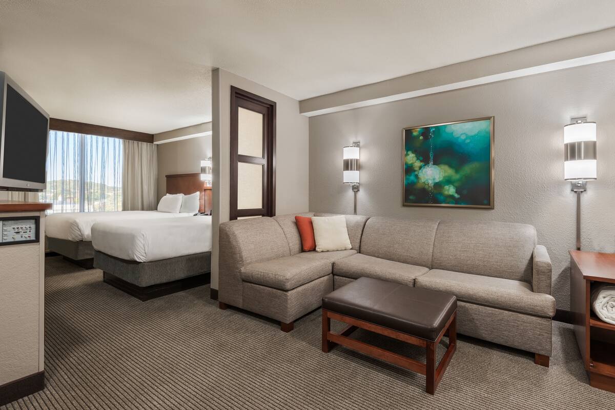 A hotel room with a bed, a sofa, a coffee table, a TV, and a painting on the wall.