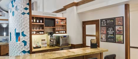 A bar area with a granite countertop, bar stools, a coffee machine, and shelves with bottles and glasses.