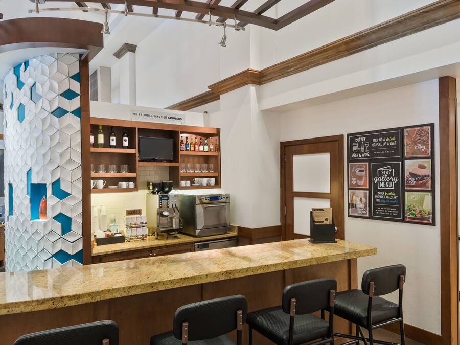 A bar area with a granite countertop, bar stools, a coffee machine, and shelves with bottles and glasses.