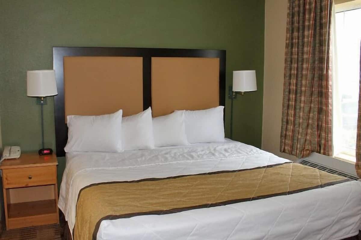 A hotel room with a bed, two bedside tables, a lamp on each table, a clock, and a window with curtains.