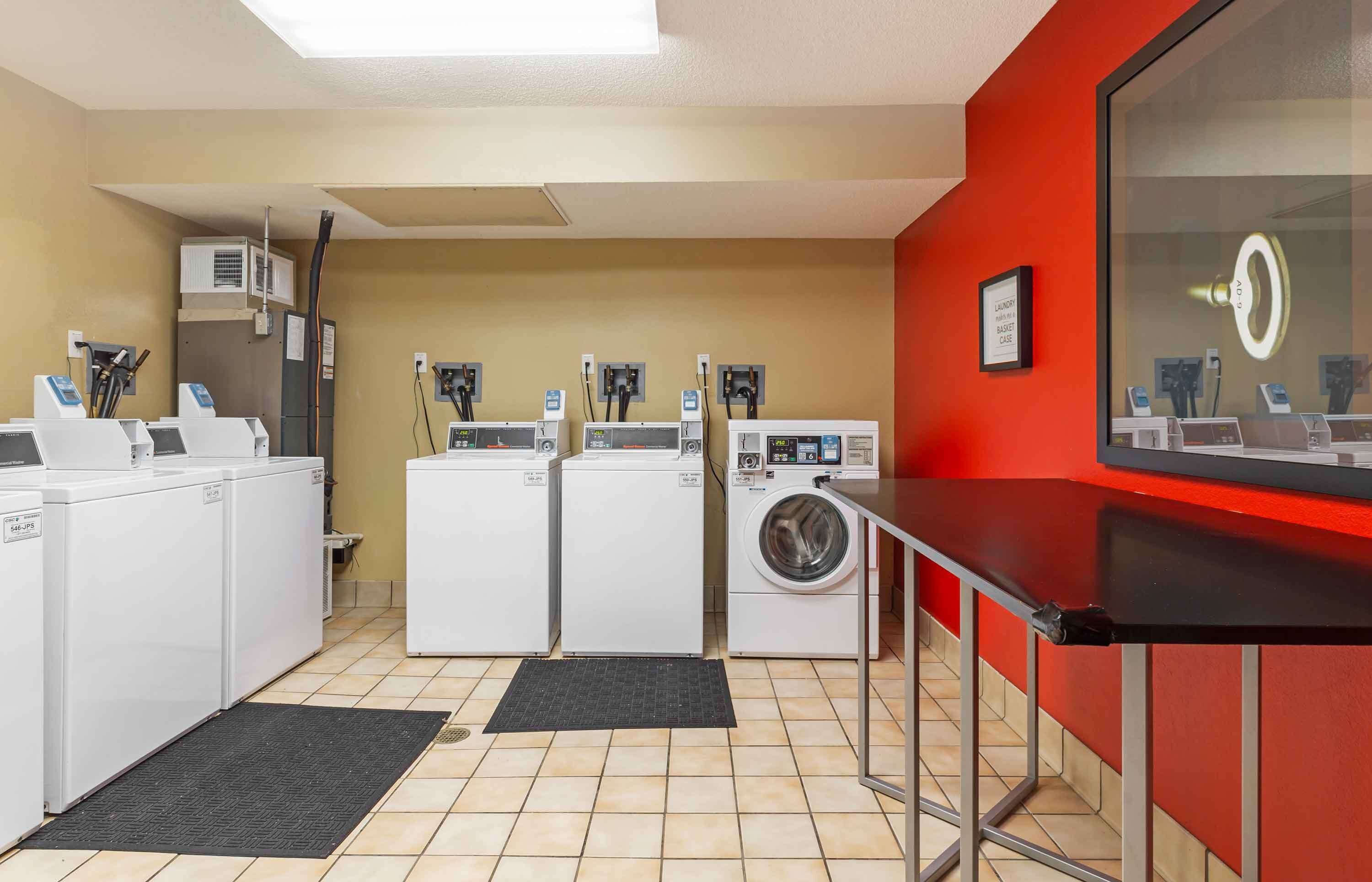 A laundry facility with multiple washing machines and dryers, a sink, and a mirror with a light.