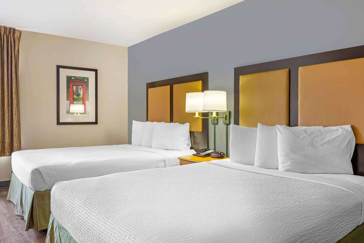 A hotel room with two beds, a framed picture on the wall, and a nightstand with a lamp.