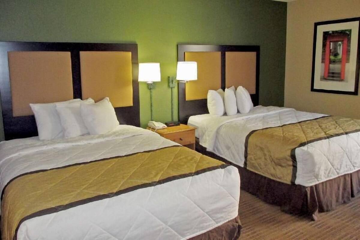 A hotel room with two beds, each with white bedding and a brown headboard. There are two bedside lamps on either side of the beds.