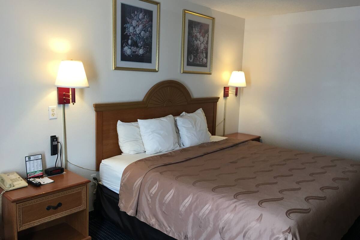 A hotel room with a wooden headboard, two bedside lamps, a telephone, and a nightstand.