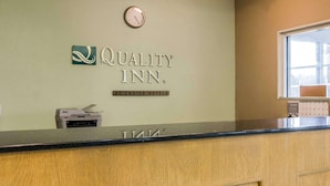 A reception desk with a clock above it, a sign reading "Quality Inn by Choice Hotels," and a window to the right. - Quality Inn Kalamazoo near Wings Stadium (Kalamazoo)
