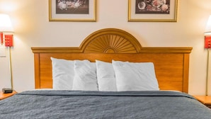 A neatly made bed with a wooden headboard, white pillows, and a grey quilt. - Quality Inn Kalamazoo near Wings Stadium (Kalamazoo)