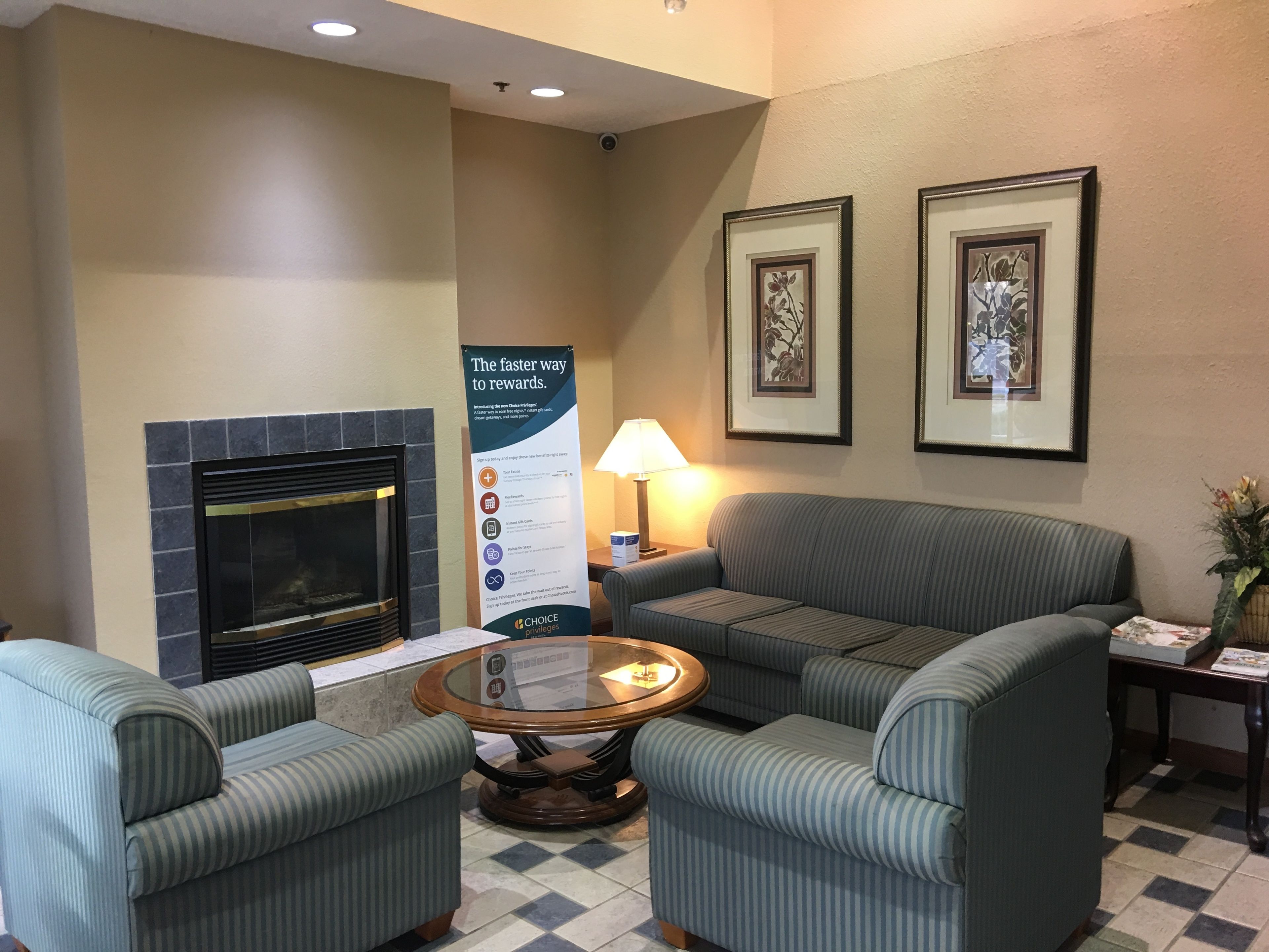 A lobby with striped armchairs, a fireplace, framed artwork, a signboard, and a table with a lamp.
