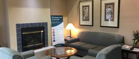 A lobby with striped armchairs, a fireplace, framed artwork, a signboard, and a table with a lamp.