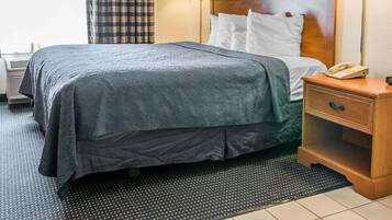 A hotel room with a bed, two bedside lamps, a nightstand with a phone, and a window with curtains.