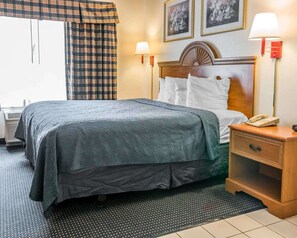 A hotel room with a bed, two bedside lamps, a nightstand with a phone, and a window with curtains.