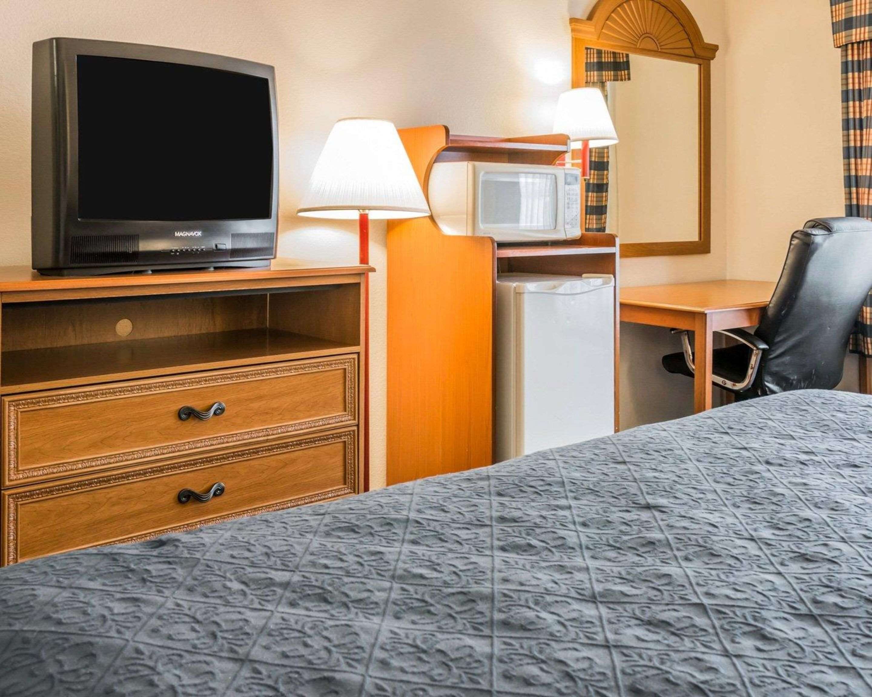 Een hotelkamer met een bed, televisie, magnetron, koelkast, bureau en stoel.