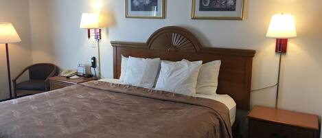 A hotel room with a large bed, two bedside lamps, a wooden headboard, and two framed floral paintings on the wall.