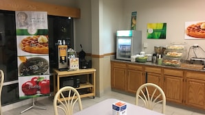 A breakfast area with a waffle maker, coffee machine, and a refrigerated display case. - Quality Inn Kalamazoo near Wings Stadium (Kalamazoo)
