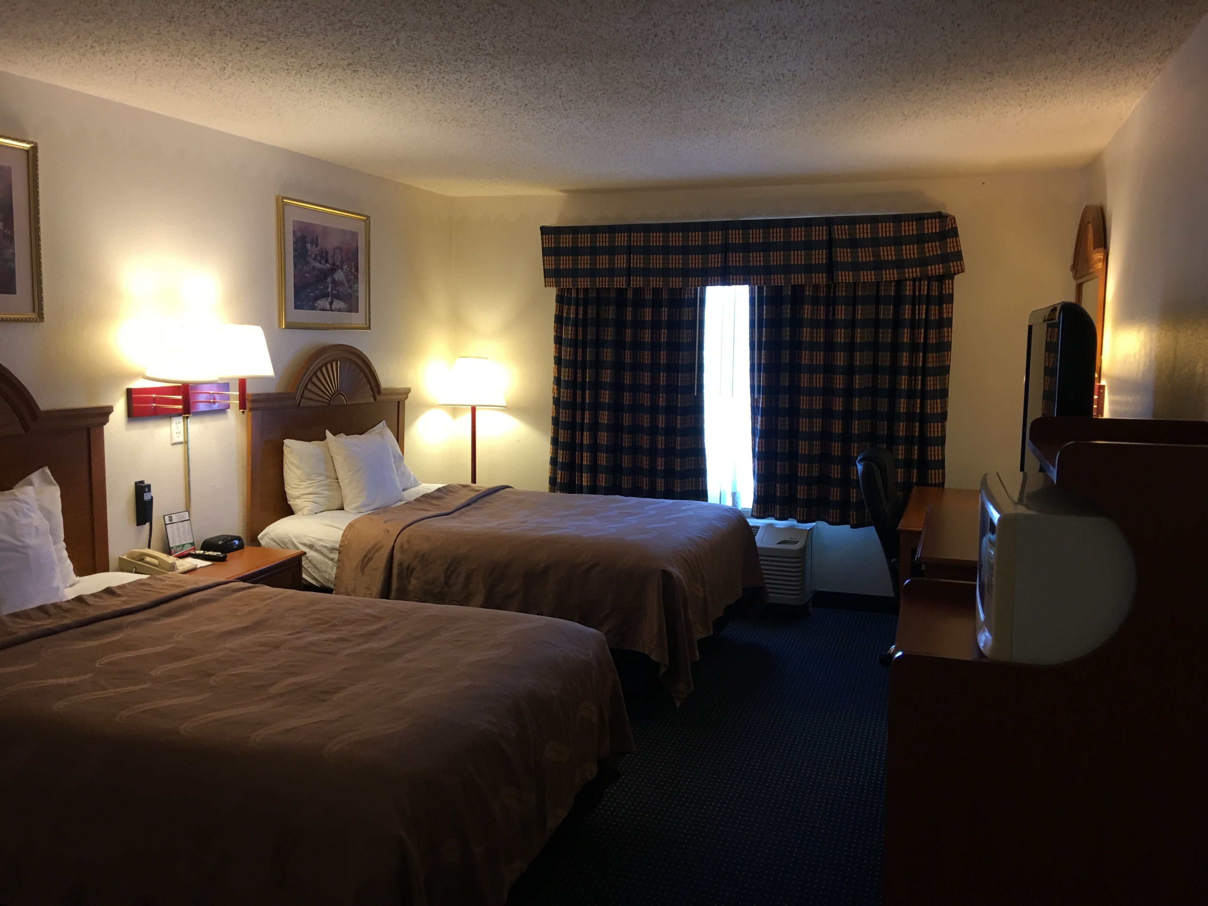 A hotel room with two beds, a desk, a chair, a television, and a window with curtains.