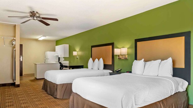 A hotel room with two beds, a kitchenette, a ceiling fan, and green walls.