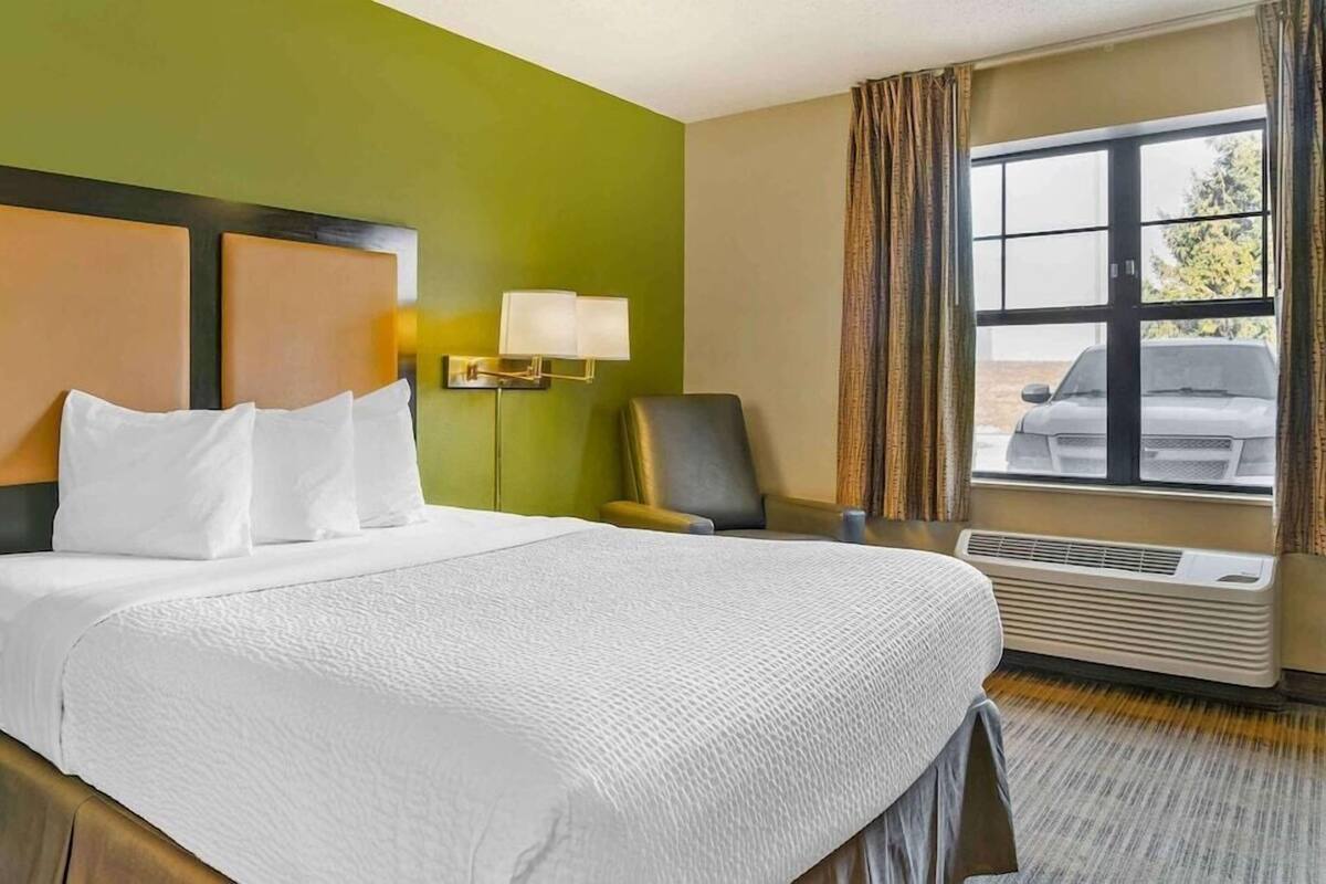A hotel room with a large bed, a chair, a lamp, and a window with curtains.