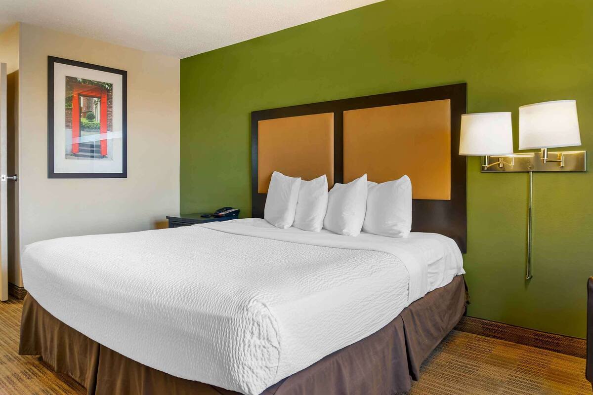 A hotel room with a large bed, a nightstand, a framed picture on the wall, and a green accent wall.