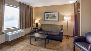 A hotel room with a sofa, a table, a lamp, a picture on the wall, and a window with curtains.