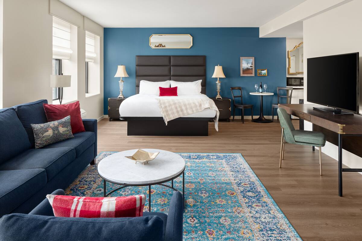 A modern hotel room with a large bed, a sofa, a desk, and a TV.