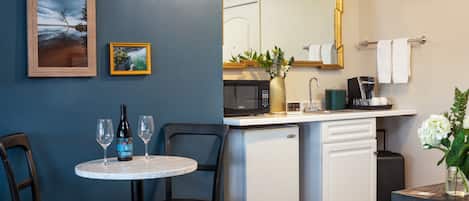 A compact kitchenette with a microwave, coffee maker, and a small refrigerator. There is a dining area with a table and chairs, and a small framed picture on the wall.