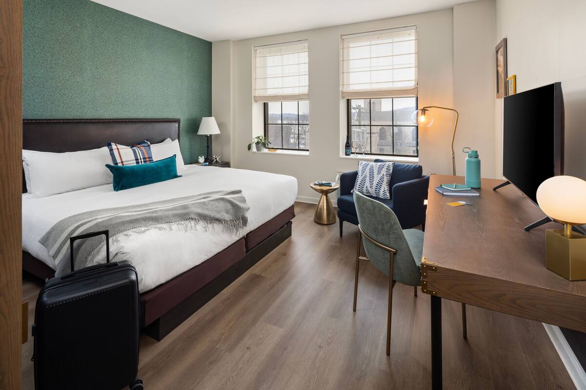 A hotel room with a bed, a desk, a chair, a TV, and a window with a view.