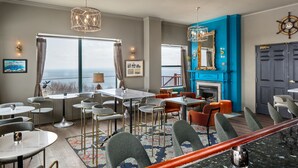 A modern dining area with round tables and chairs, a blue accent wall, and a view of the sea. - Landmark Inn (Marquette)