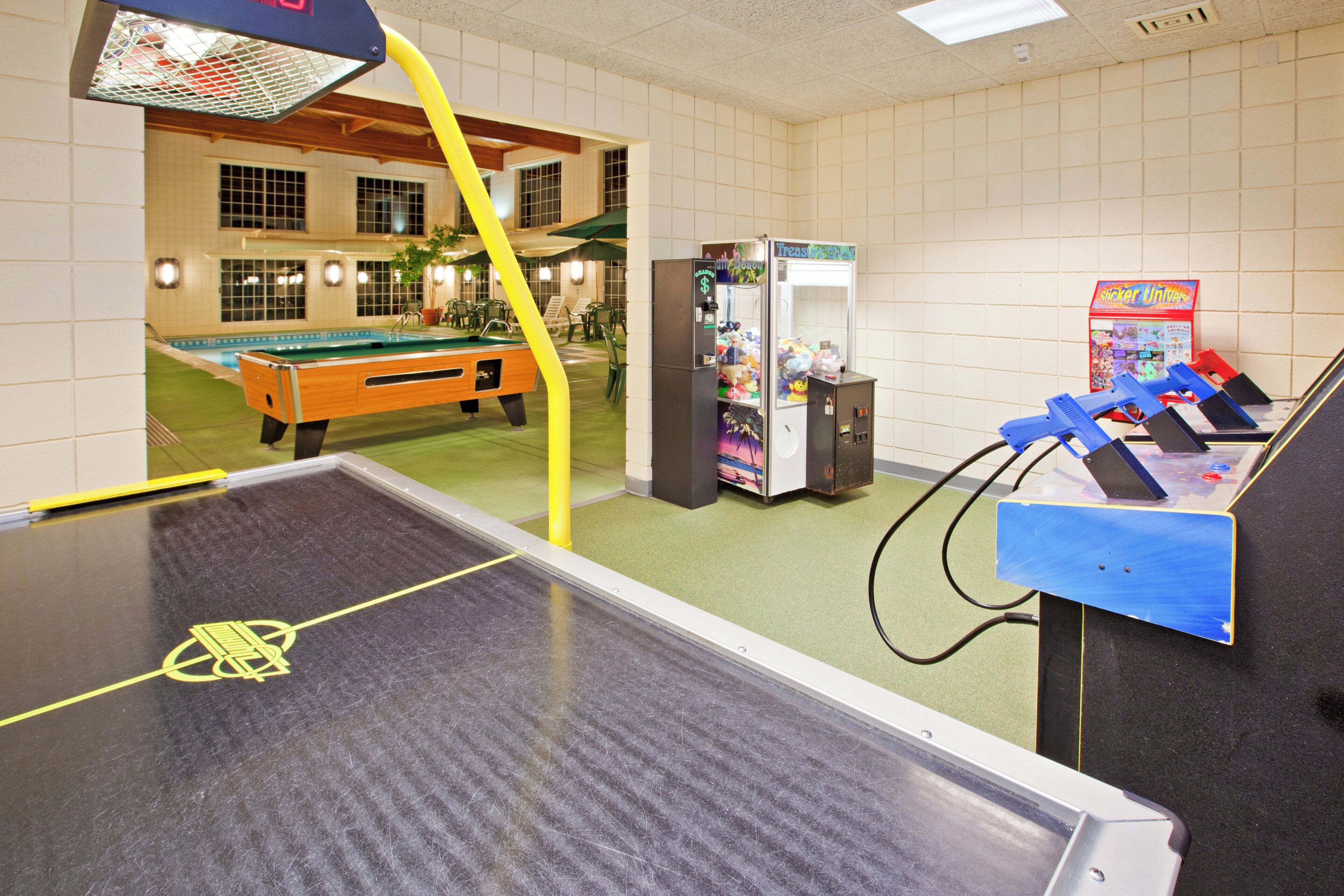 A pool table with a yellow barrier, a claw machine, and a vending machine in a room with tiled walls and a pool table visible in the background.