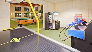 A pool table with a yellow barrier, a claw machine, and a vending machine in a room with tiled walls and a pool table visible in the background.