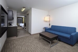 Ein Hotelzimmer mit einer Couch, einem kleinen Tisch, einer Lampe, einer Küchenzeile und einer Tür zu einem Badezimmer.