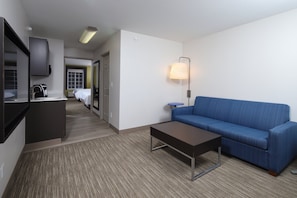 A hotel room with a kitchenette, a blue sofa, a coffee table, and a lamp. - Holiday Inn Express Grand Rapids SW by IHG (Grandville)