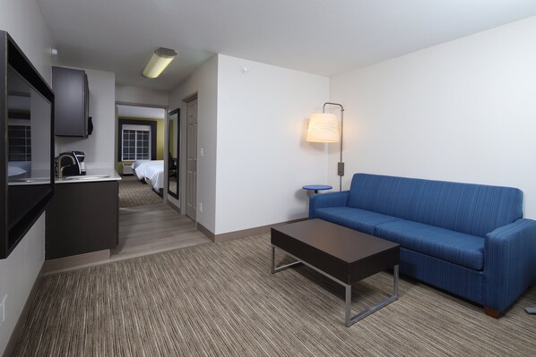 A hotel room with a kitchenette, a blue sofa, a coffee table, and a lamp. - Holiday Inn Express Grand Rapids SW by IHG (Grandville)